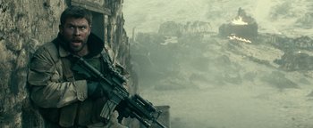 Movie still from “12 Strong” (2018), directed by Nicolai Fuglsig – A man holding a gun while standing next to a wall; Medium shot, Low angle