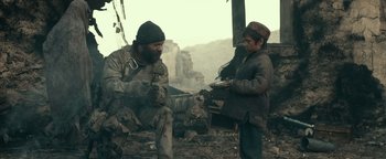 Movie still from “12 Strong” (2018), directed by Nicolai Fuglsig – A man sitting next to a young boy in a field; Medium shot, Low angle