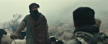 Movie still from “12 Strong” (2018), directed by Nicolai Fuglsig – A man with a long beard standing next to another man in a field; Medium shot, Over the shoulder angle