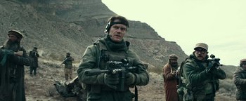 Movie still from “12 Strong” (2018), directed by Nicolai Fuglsig – A man holding a gun while standing on top of a hill; Medium shot, Over the shoulder angle