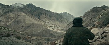 Movie still from “12 Strong” (2018), directed by Nicolai Fuglsig – A man in a camouflage jacket standing in front of a mountain range; Wide shot, Low angle