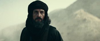 Movie still from “12 Strong” (2018), directed by Nicolai Fuglsig – A man with a long beard wearing a black turban; Close Up shot, Over the shoulder angle