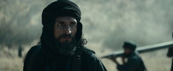 Movie still from “12 Strong” (2018), directed by Nicolai Fuglsig – A man with a beard is wearing a black turban; Close Up shot, Over the shoulder angle