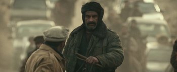 Movie still from “12 Strong” (2018), directed by Nicolai Fuglsig – A man in a fur coat and a hat is holding a stick; Medium shot, Over the shoulder angle