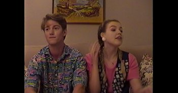 Movie still from “Dramarama” (2020), directed by Jonathan Wysocki – A man and a woman sitting next to each other in a room; Medium shot, High angle