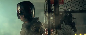 Movie still from “Dredd” (2012), directed by Pete Travis – A person in a helmet and a suit is standing in front of a stack of plastic bottles; Close Up shot, Low angle