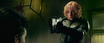 Movie still from “Dredd” (2012), directed by Pete Travis – A woman holding a gun while wearing gloves; Medium shot, Over the shoulder angle