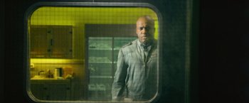 Movie still from “Dredd” (2012), directed by Pete Travis – A man standing in front of a glass window; Medium shot, Over the shoulder angle