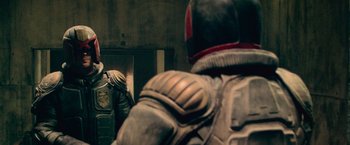 Movie still from “Dredd” (2012), directed by Pete Travis – A man in a helmet is standing in front of a mirror; Medium shot, Over the shoulder angle