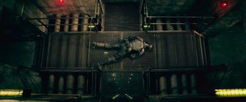 Movie still from “Dredd” (2012), directed by Pete Travis – A man is hanging upside down on a metal structure; Wide shot, Overhead angle