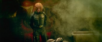 Movie still from “Dredd” (2012), directed by Pete Travis – A man in a leather suit standing in front of a smoke filled room; Medium shot, Over the shoulder angle