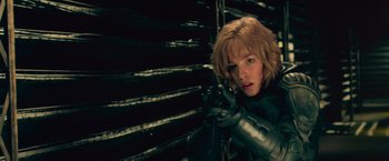 Movie still from “Dredd” (2012), directed by Pete Travis – A woman in a metal suit is holding a gun; Close Up shot, Low angle