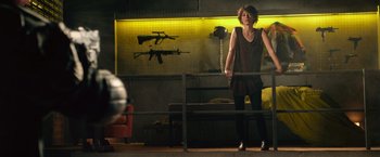 Movie still from “Dredd” (2012), directed by Pete Travis – A woman standing in front of a wall with a gun hanging on the wall; Wide shot, Low angle