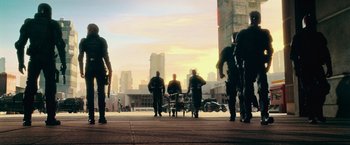 Movie still from “Dredd” (2012), directed by Pete Travis – A group of men standing on top of a sidewalk near a building; Wide shot, Low angle