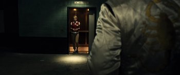 Movie still from “Drive” (2011), directed by Nicolas Winding Refn – A man in a red jacket standing in an elevator; Wide shot, Low angle