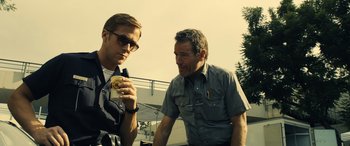 Movie still from “Drive” (2011), directed by Nicolas Winding Refn – A man and a man standing next to each other holding a cup; Medium shot, Low angle