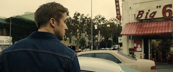 Movie still from “Drive” (2011), directed by Nicolas Winding Refn – A man standing on the side of the road next to a car; Close Up shot, Over the shoulder angle