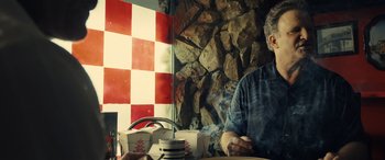 Movie still from “Drive” (2011), directed by Nicolas Winding Refn – A man sitting at a table in front of a brick wall; Medium shot, Low angle