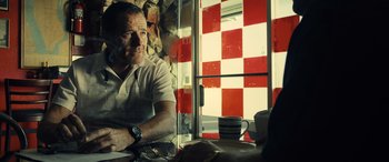 Movie still from “Drive” (2011), directed by Nicolas Winding Refn – A man sitting at a table in front of a checkerboard window; Medium shot, Over the shoulder angle