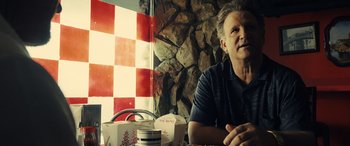 Movie still from “Drive” (2011), directed by Nicolas Winding Refn – A man sitting in front of a checkerboard wall; Close Up shot, Over the shoulder angle