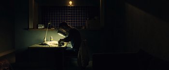Movie still from “Drive” (2011), directed by Nicolas Winding Refn – A man sitting at a table in a dark room; Wide shot, Low angle