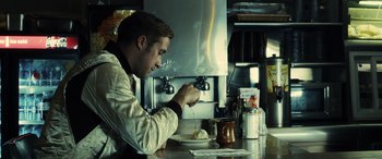 Movie still from “Drive” (2011), directed by Nicolas Winding Refn – A man sitting at a table with a plate of food; Medium shot, Over the shoulder angle