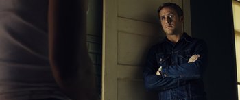 Movie still from “Drive” (2011), directed by Nicolas Winding Refn – A man standing in front of a wall with his arms crossed; Close Up shot, Over the shoulder angle