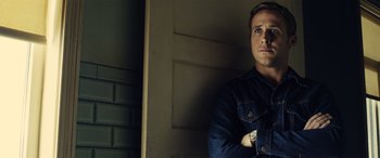 Movie still from “Drive” (2011), directed by Nicolas Winding Refn – A man standing in front of a wall with his arms crossed; Close Up shot, Low angle
