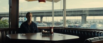 Movie still from “Drive” (2011), directed by Nicolas Winding Refn – A man sitting at a table in front of a large window; Medium shot, Over the shoulder angle