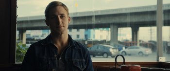 Movie still from “Drive” (2011), directed by Nicolas Winding Refn – A man sitting in front of a window with cars in the background; Close Up shot, Over the shoulder angle