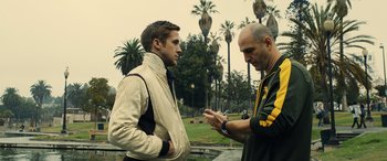 Movie still from “Drive” (2011), directed by Nicolas Winding Refn – Two men are standing in a park looking at a cell phone; Close Up shot, Over the shoulder angle
