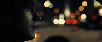 Movie still from “Drive” (2011), directed by Nicolas Winding Refn – A man's face in front of blurry lights; Extreme Close Up shot, Low angle