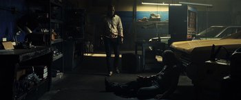 Movie still from “Drive” (2011), directed by Nicolas Winding Refn – A man standing in a room next to a man laying on the ground; Wide shot, Over the shoulder angle