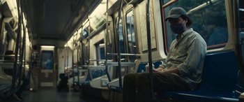 Movie still from “Dumb Money” (2023), directed by Craig Gillespie – A man sitting on a subway train while wearing a hat; Wide shot, Low angle