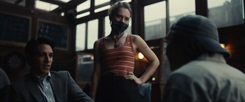 Movie still from “Dumb Money” (2023), directed by Craig Gillespie – A woman wearing a red and white striped shirt and a black face mask; Medium shot, Low angle