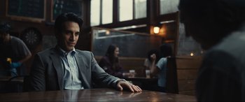 Movie still from “Dumb Money” (2023), directed by Craig Gillespie – A man sitting at a table in front of other people in a restaurant; Medium shot, Over the shoulder angle