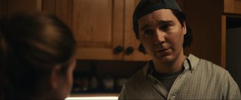 Movie still from “Dumb Money” (2023), directed by Craig Gillespie – A young man wearing a baseball cap in a kitchen; Close Up shot, Over the shoulder angle