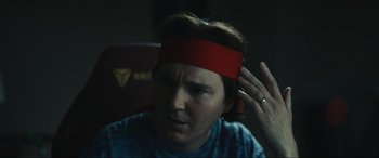 Movie still from “Dumb Money” (2023), directed by Craig Gillespie – A man with a red headband is sitting in a chair; Close Up shot, Over the shoulder angle