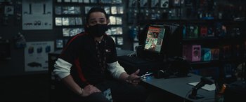 Movie still from “Dumb Money” (2023), directed by Craig Gillespie – A person sitting in front of a computer holding a cell phone; Medium shot, High angle