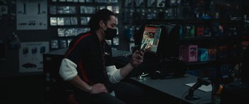 Movie still from “Dumb Money” (2023), directed by Craig Gillespie – A man sitting at a desk looking at a phone; Medium shot, Over the shoulder angle