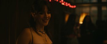 Movie still from “Dumb Money” (2023), directed by Craig Gillespie – A beautiful young lady smiling for the camera with lights in the background; Close Up shot, Over the shoulder angle