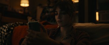 Movie still from “Dumb Money” (2023), directed by Craig Gillespie – A woman looking at her cell phone while sitting on a couch; Close Up shot, Over the shoulder angle