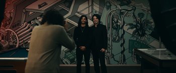 Movie still from “Dumb Money” (2023), directed by Craig Gillespie – A man taking a picture of two men in front of a mural; Wide shot, Low angle