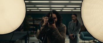 Movie still from “Dumb Money” (2023), directed by Craig Gillespie – A man taking a picture with a camera in a room; Medium shot, Over the shoulder angle