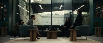 Movie still from “Dumb Money” (2023), directed by Craig Gillespie – A man and a woman sitting on a couch in front of a window; Wide shot, Over the shoulder angle