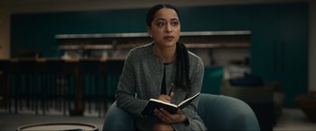 Movie still from “Dumb Money” (2023), directed by Craig Gillespie – A woman sitting in a chair writing in a notebook; Medium shot, Over the shoulder angle