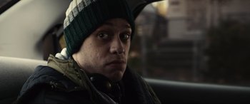 Movie still from “Dumb Money” (2023), directed by Craig Gillespie – A man wearing a green hat sitting in the back of a car; Close Up shot, Low angle