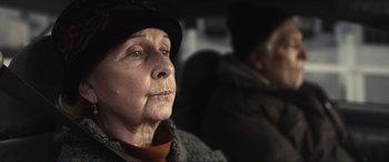 Movie still from “Dumb Money” (2023), directed by Craig Gillespie – An older woman sitting in the back of a car; Close Up shot, Over the shoulder angle