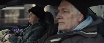 Movie still from “Dumb Money” (2023), directed by Craig Gillespie – An older man and woman in the back seat of a car; Close Up shot, Over the shoulder angle