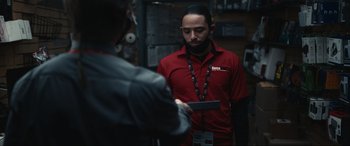 Movie still from “Dumb Money” (2023), directed by Craig Gillespie – A man in a red shirt is holding a cell phone; Medium shot, Over the shoulder angle